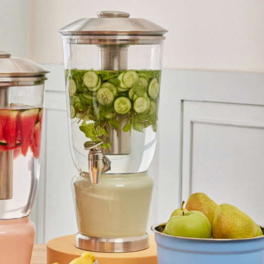 Mellow Sage Luminique dispenser in Mint Green filled with water infused with fresh green cucumbers and leaves set alongside healthy pears